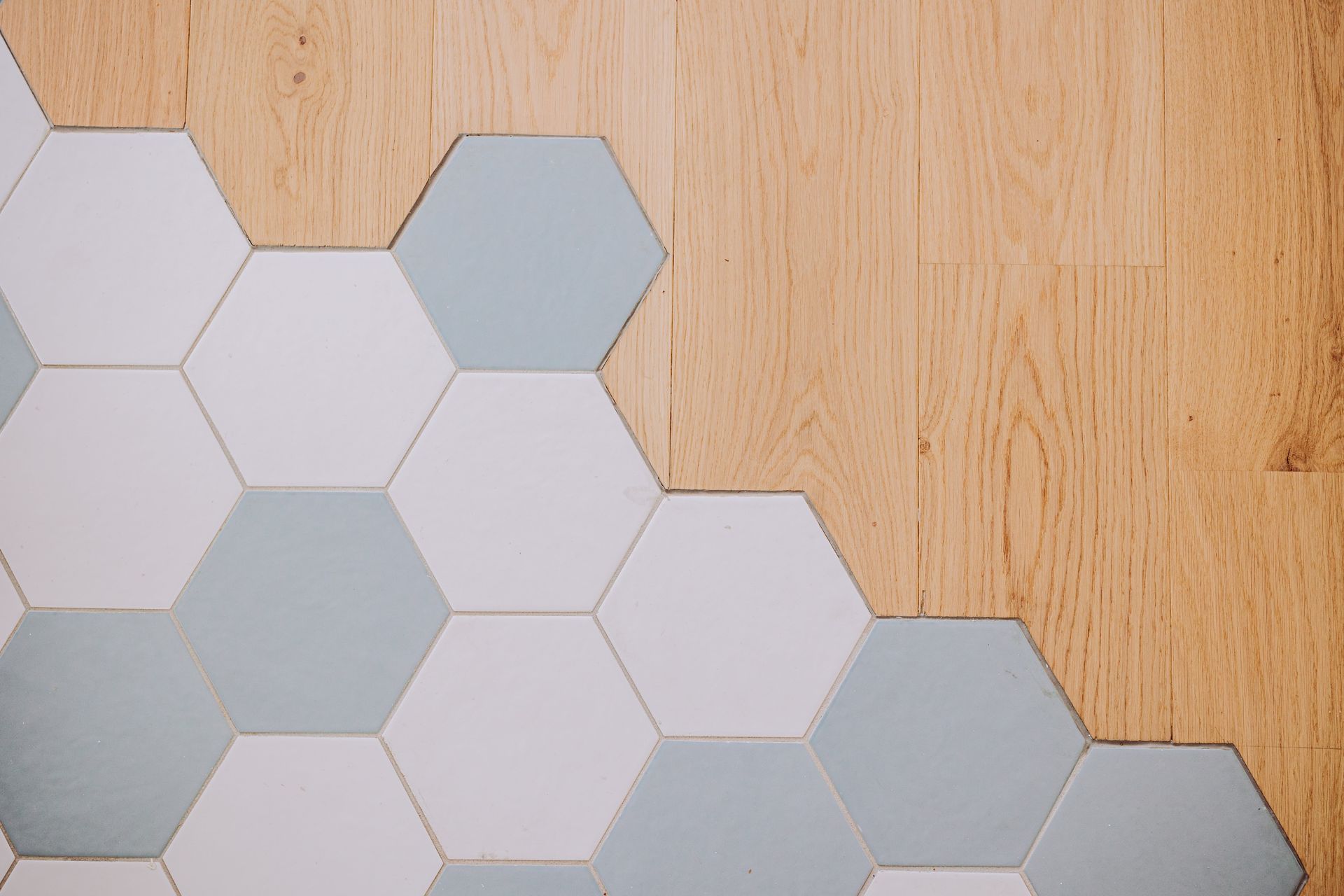 Une transition entre un parquet clair et un motif de carreaux hexagonaux blancs et bleu pâle.