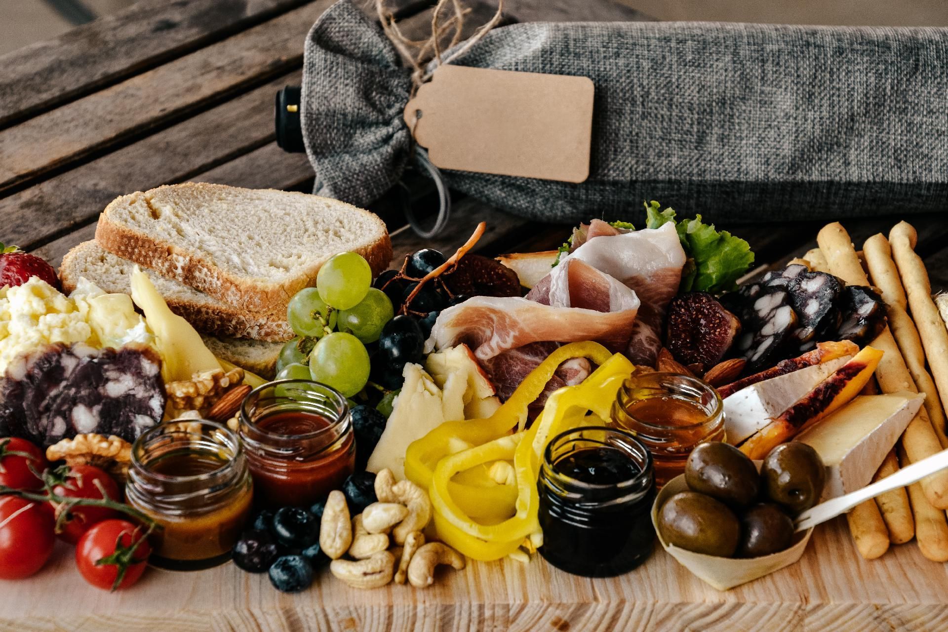 Eine Wurstplatte mit Brot, Käse, Fleisch, Obst, Nüssen, Oliven und Konfitüren, dazu eine Flasche Wein in einer Tüte.