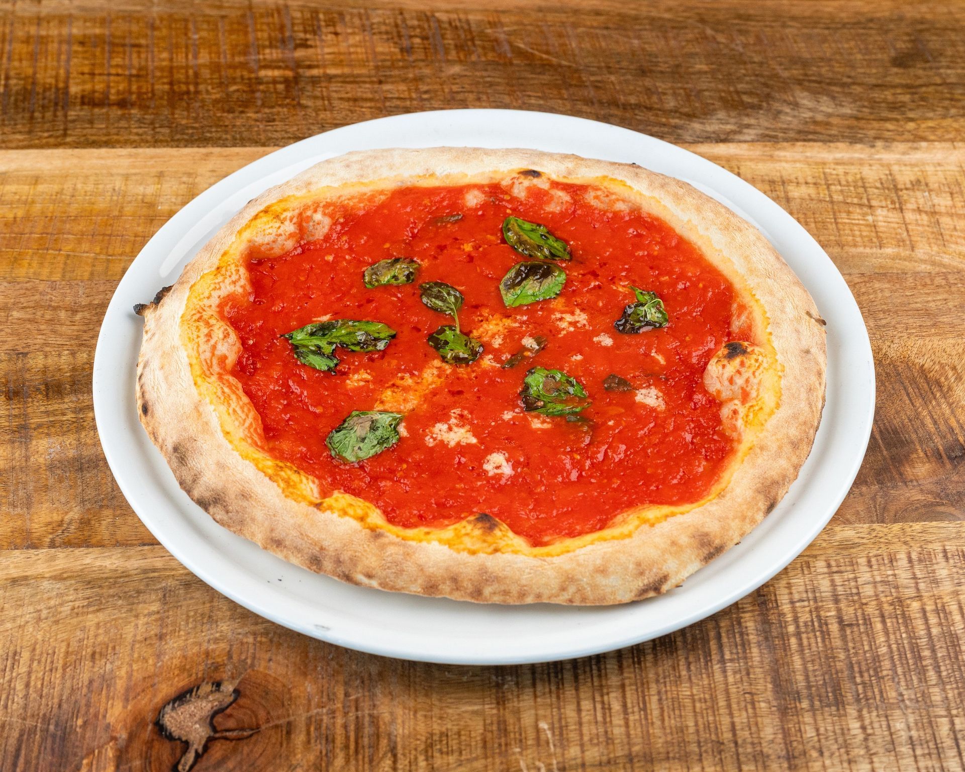 Pizza mit Tomatensoße und Basilikum auf einem weißen Teller, angerichtet auf einem Holztisch.