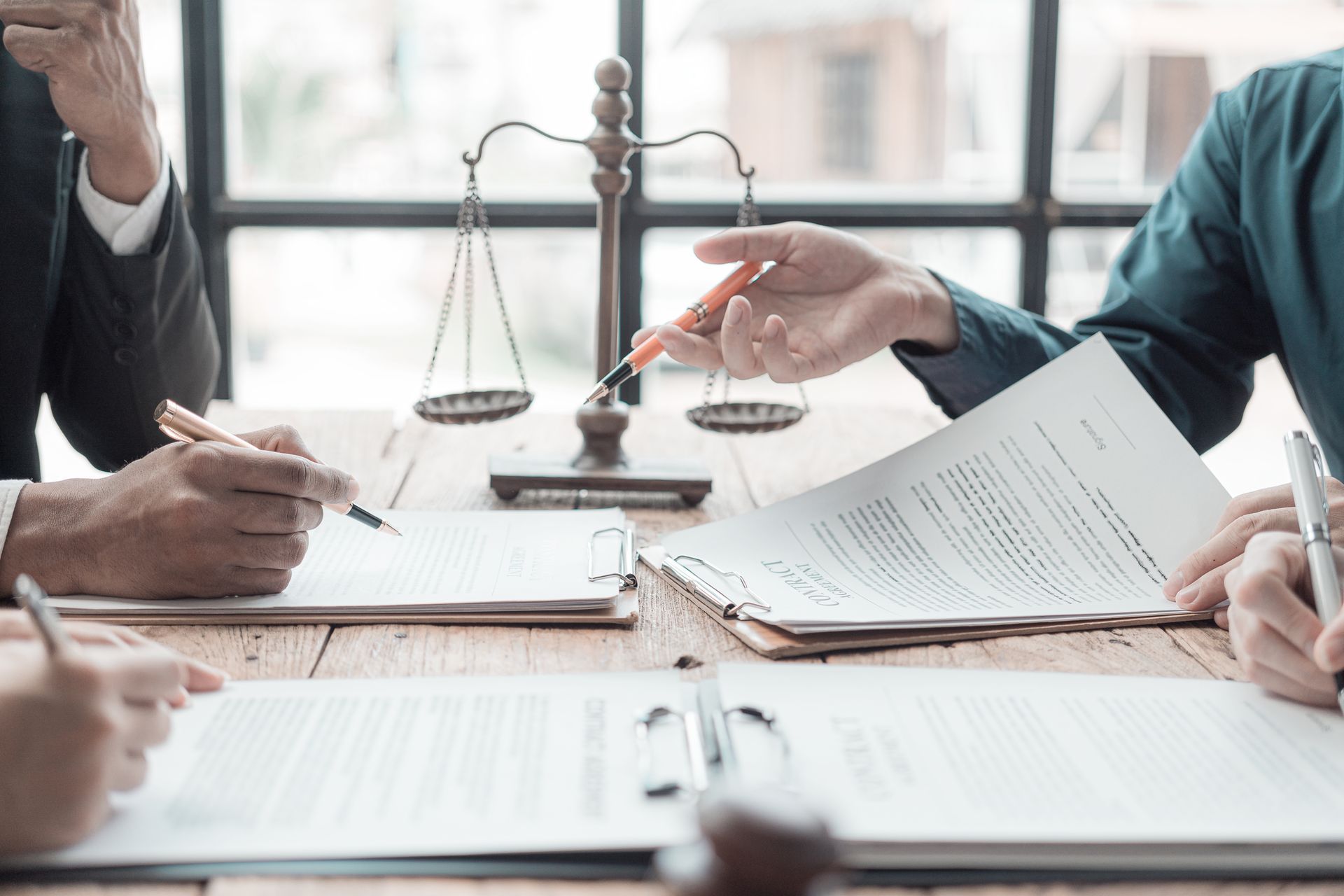 Varias personas revisan documentos en una mesa. Sobre la mesa hay una balanza de la justicia, que indica el contexto legal.