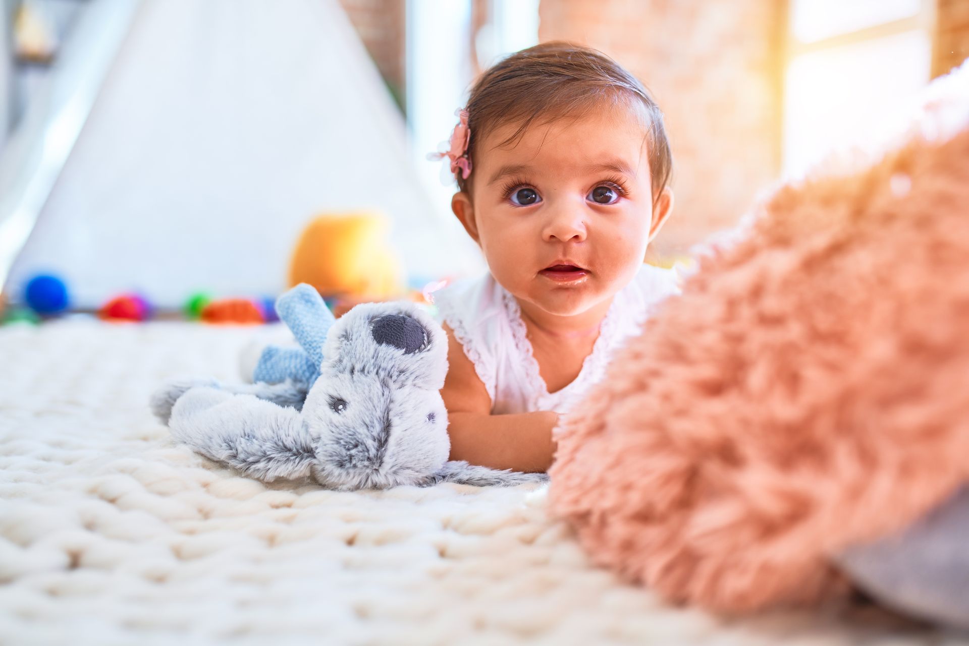 Un bébé sur le ventre avec un doudou.