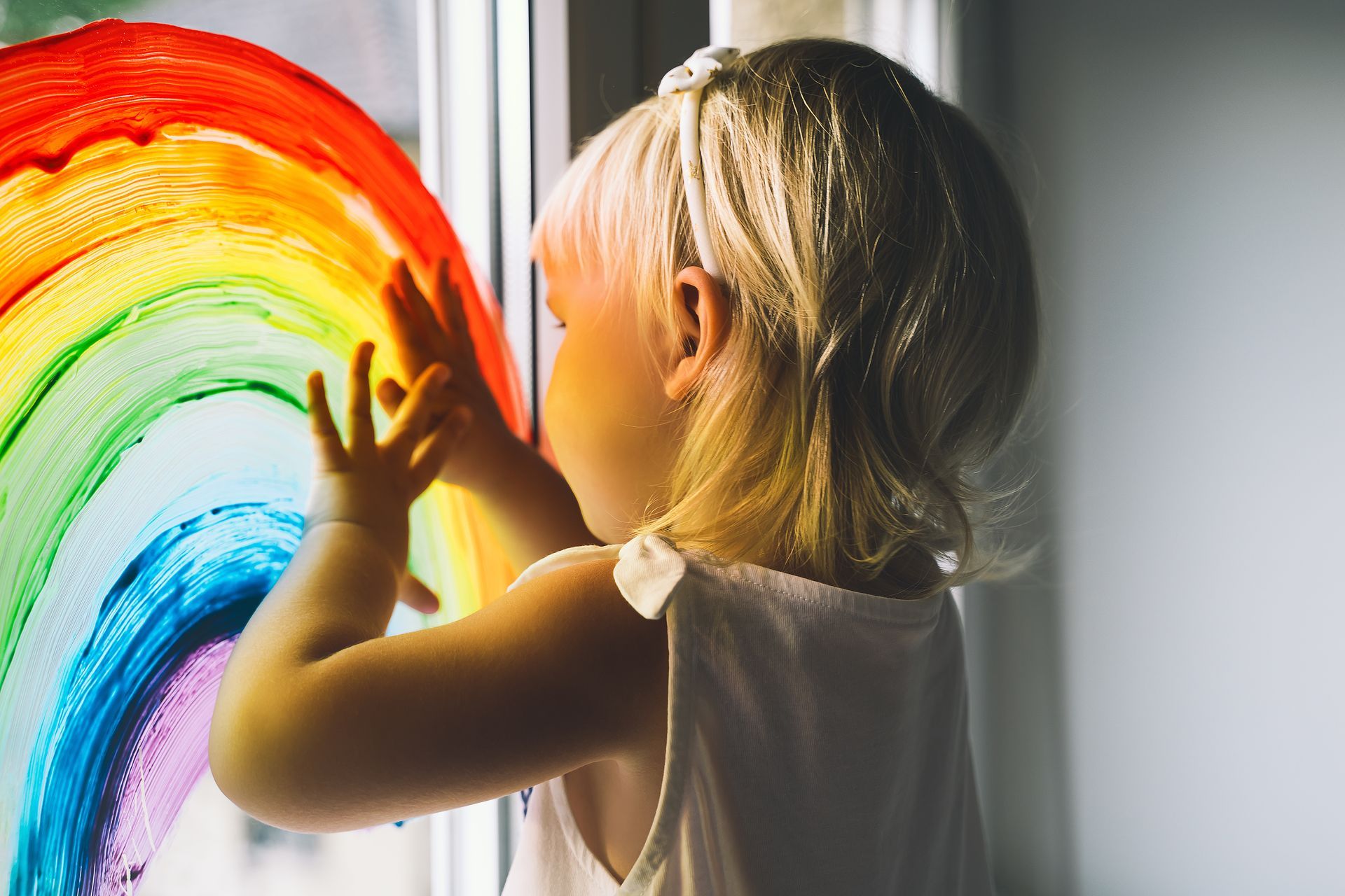 Une fillette posant ses mains sur un arc-en-ciel sur une vitre.