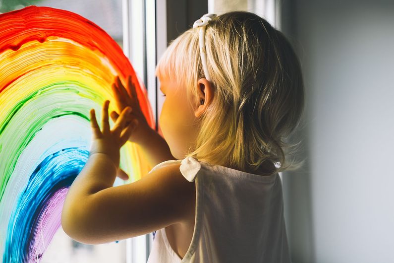 Une fillette posant ses mains sur un arc-en-ciel sur une vitre.
