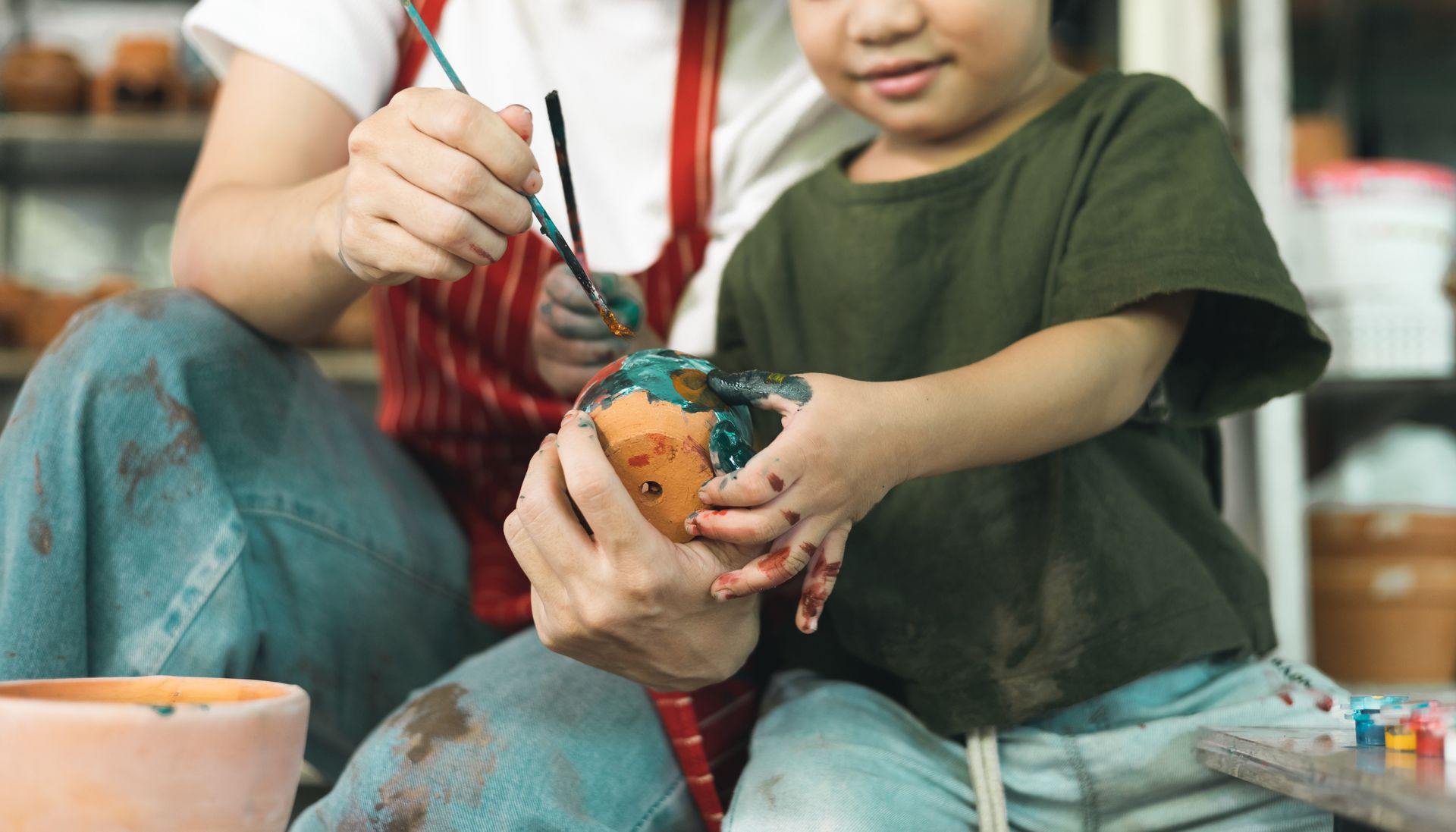 Un enfant et un adulte peignant un pot de fleur.