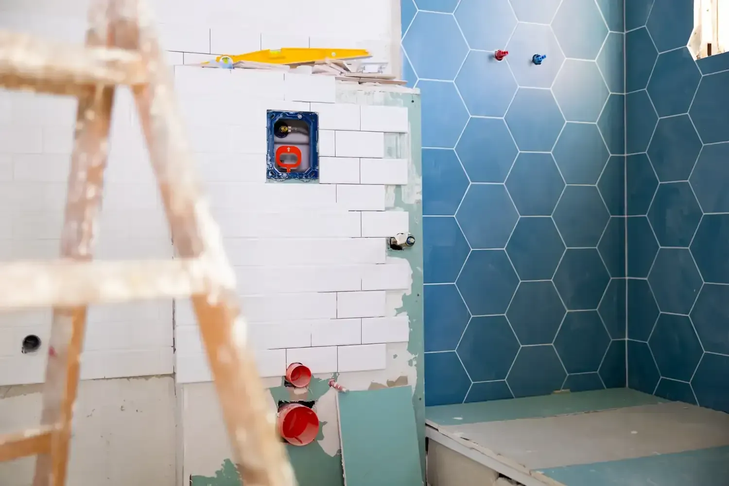 Un baño en construcción con azulejos blancos tipo metro, azulejos hexagonales azules y tuberías.