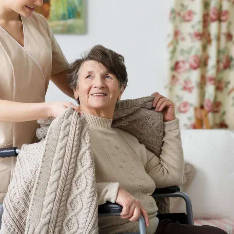 Una anciana en silla de ruedas está siendo ayudada por una enfermera.