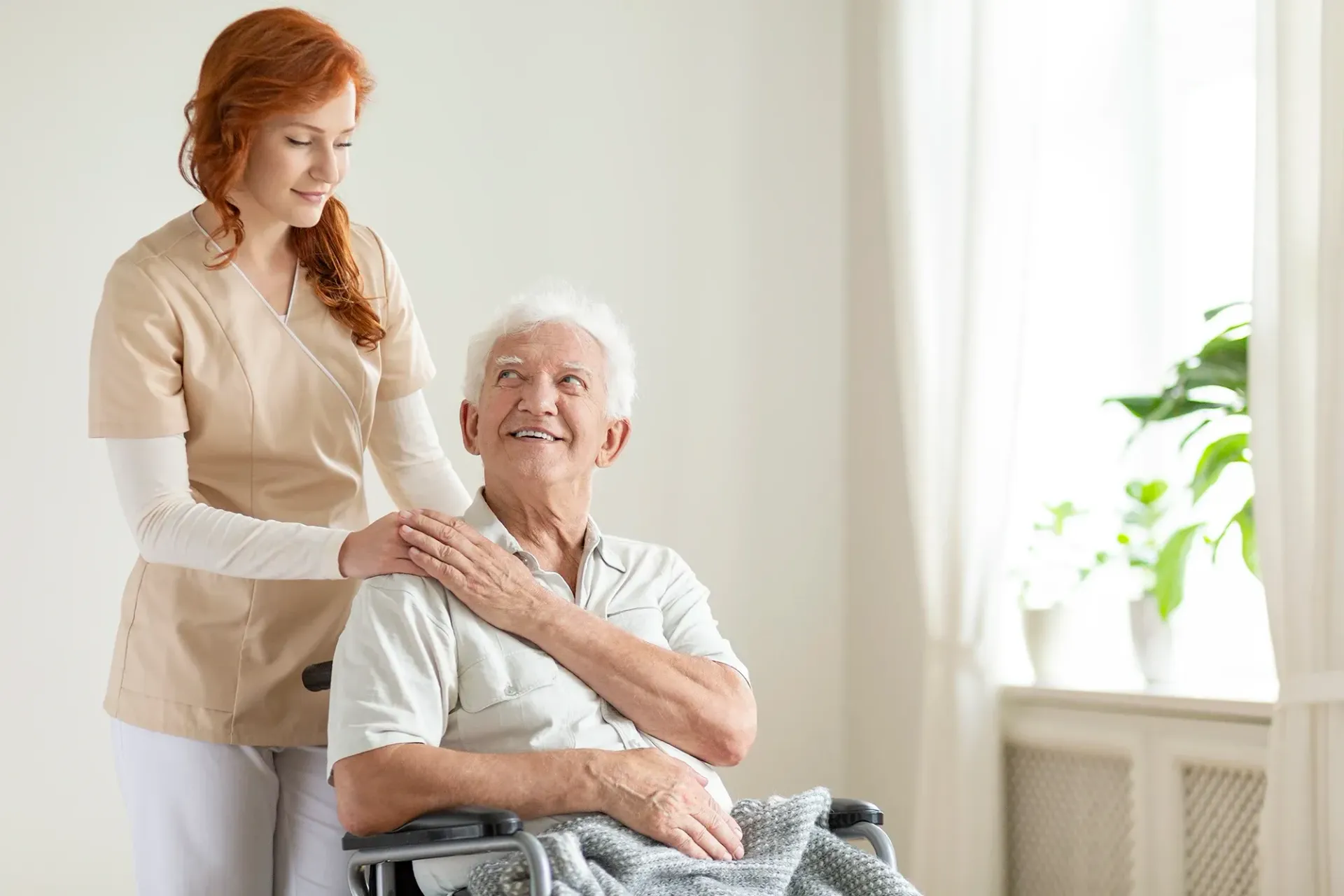 Una enfermera está de pie junto a un anciano en silla de ruedas.