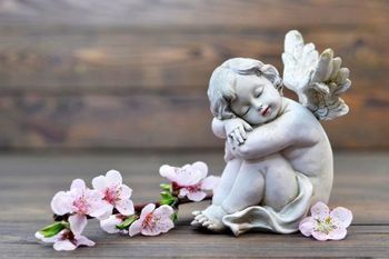Una estatua de un ángel durmiendo junto a flores rosas sobre una mesa de madera.
