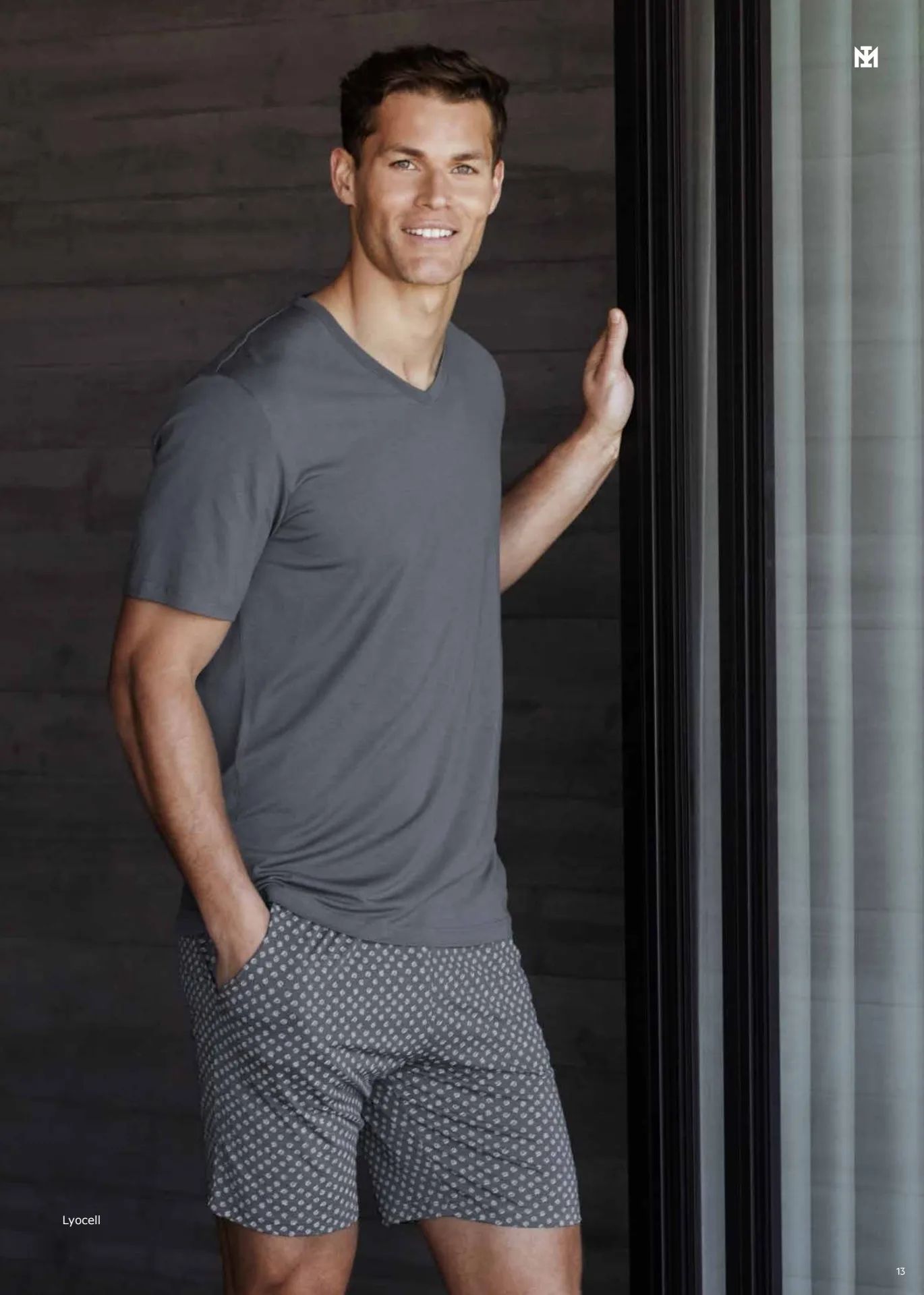 Un hombre que lleva una camiseta gris y pantalones cortos está parado frente a una ventana.