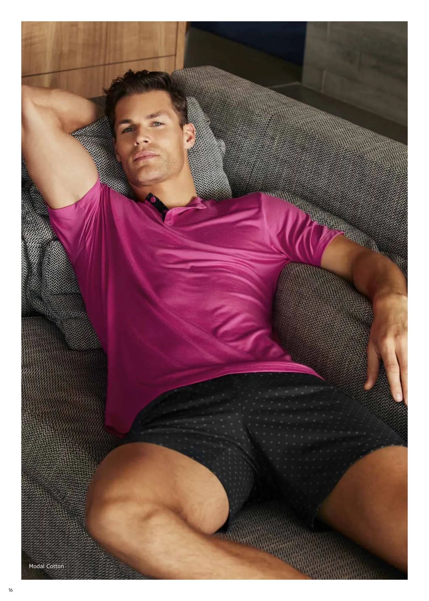 Un hombre con una camisa rosa y pantalones cortos negros está acostado en un sofá.