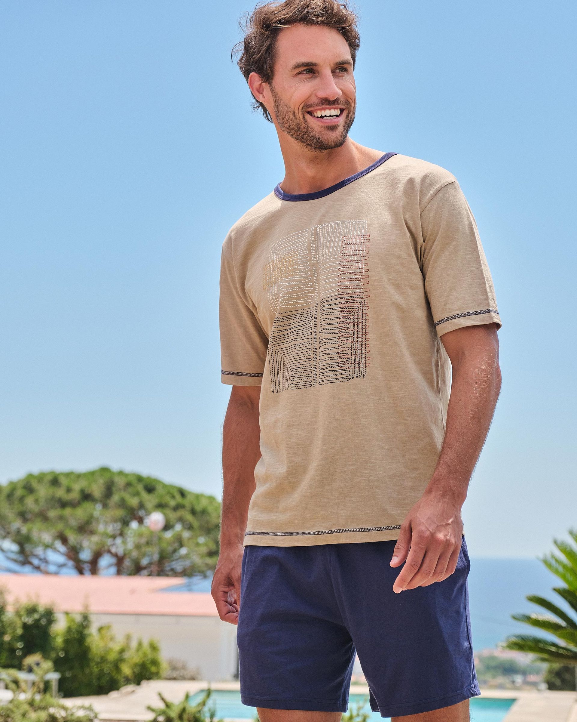 Un hombre que viste una camisa color canela y pantalones cortos azules está parado frente a una piscina.