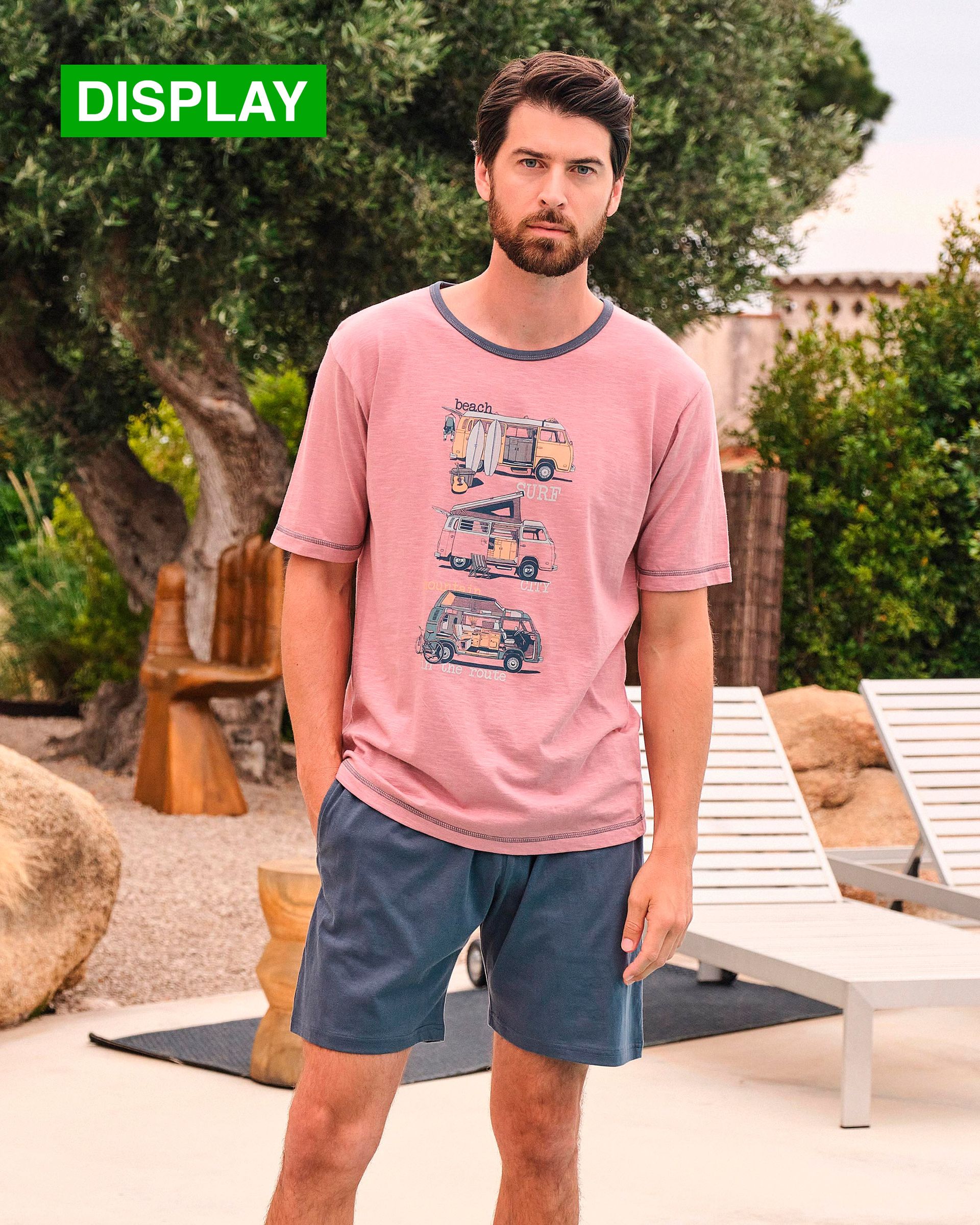 Un hombre vestido con una camisa rosa y pantalones cortos azules está parado frente a una piscina.