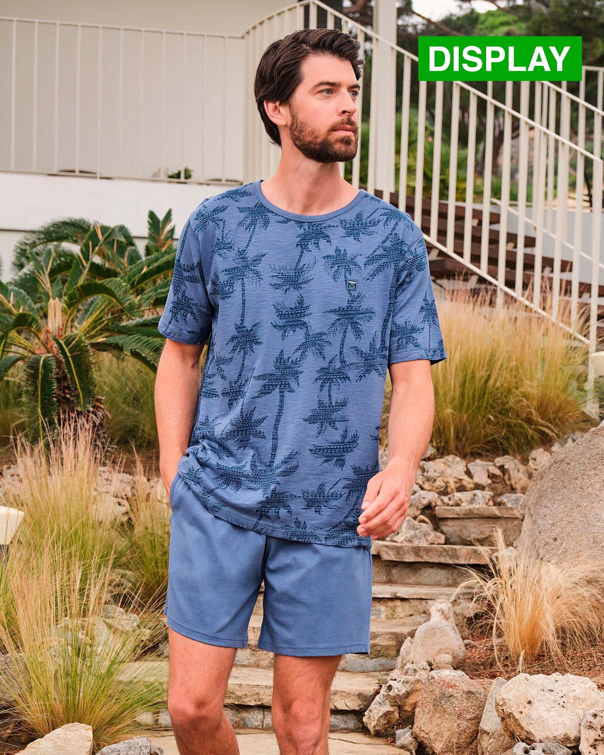 Un hombre con barba lleva una camisa azul y pantalones cortos.