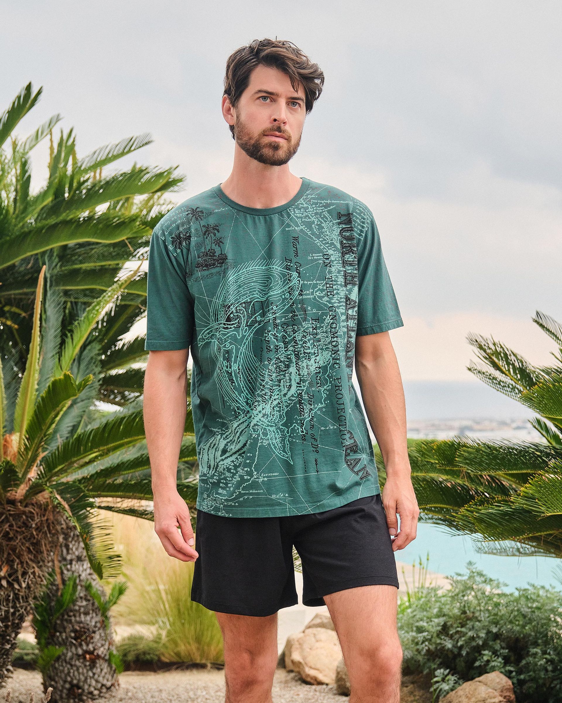 Un hombre que viste una camiseta verde y pantalones cortos negros está parado frente a una palmera.