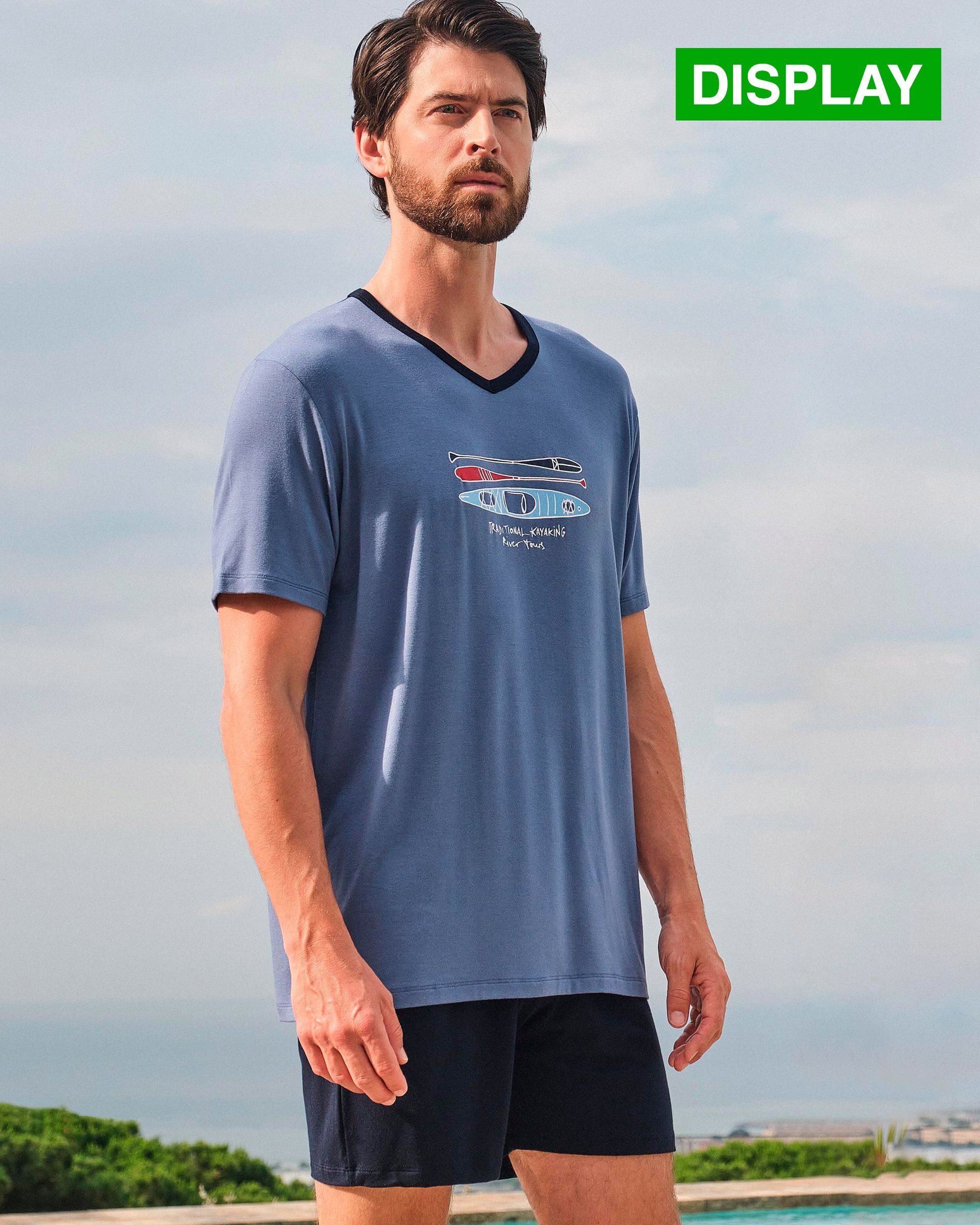 Un hombre vestido con una camisa azul y pantalones cortos negros está parado frente a una piscina.