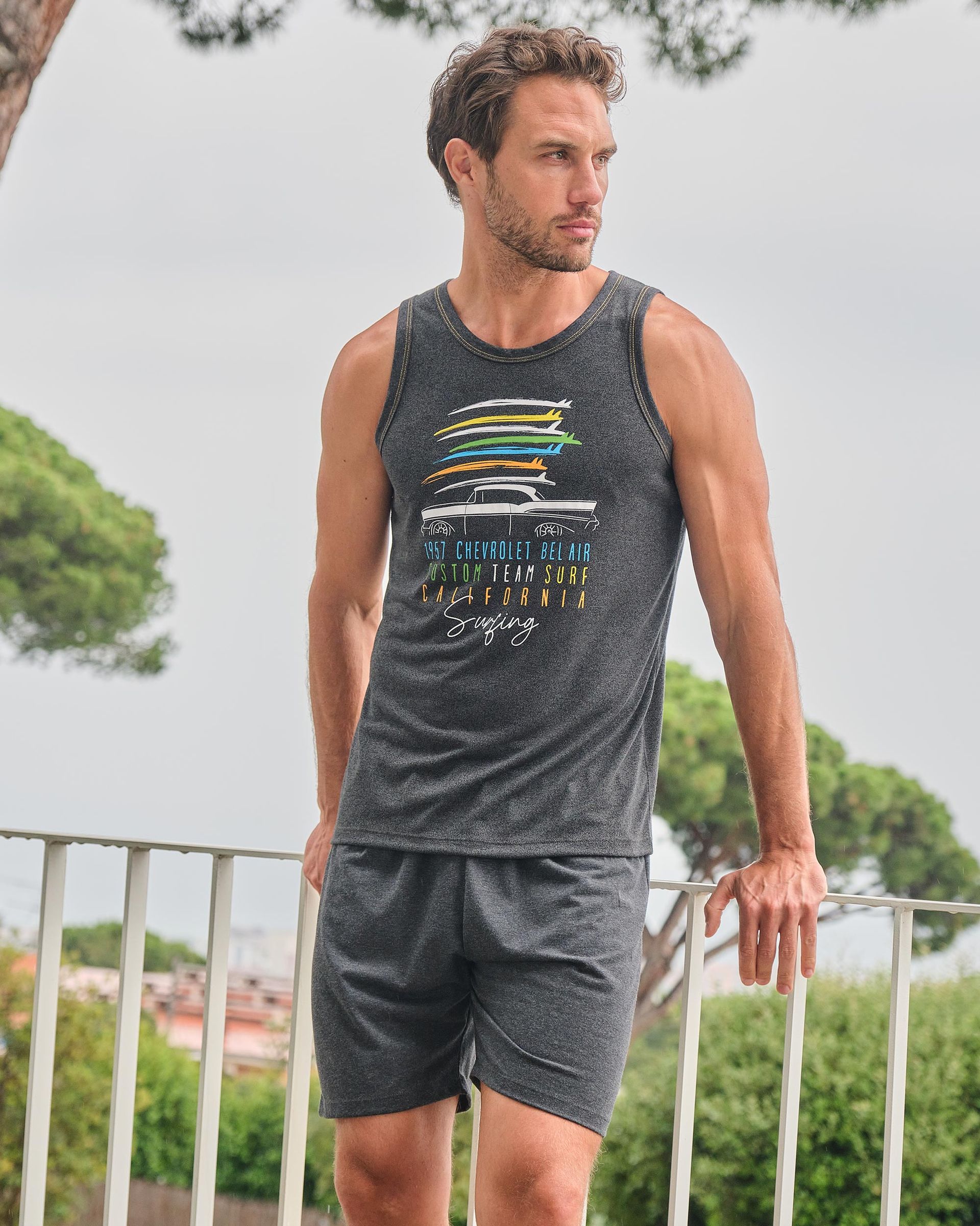 Un hombre vestido con una camiseta sin mangas y pantalones cortos está de pie sobre una barandilla.