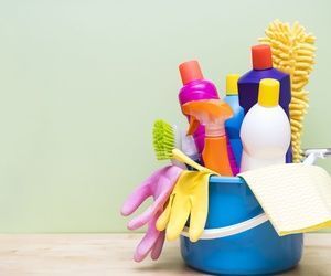 Balde azul lleno de productos de limpieza: botellas, guantes, cepillo y un paño.