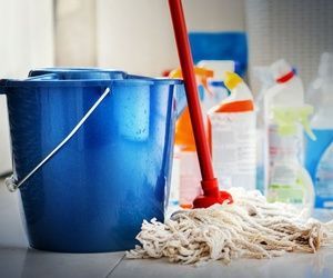 Cubo azul, trapeador y productos de limpieza sobre un piso de baldosas.