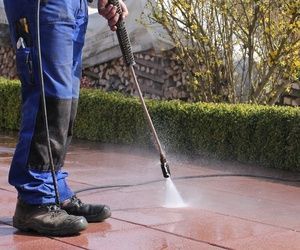 Persona con mono azul lavando a presión un patio de ladrillos rojos.