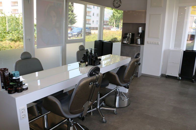 Saloneinrichtung: weißer Tisch mit Stühlen, Produkten, große Fenster, Kaffeestation.