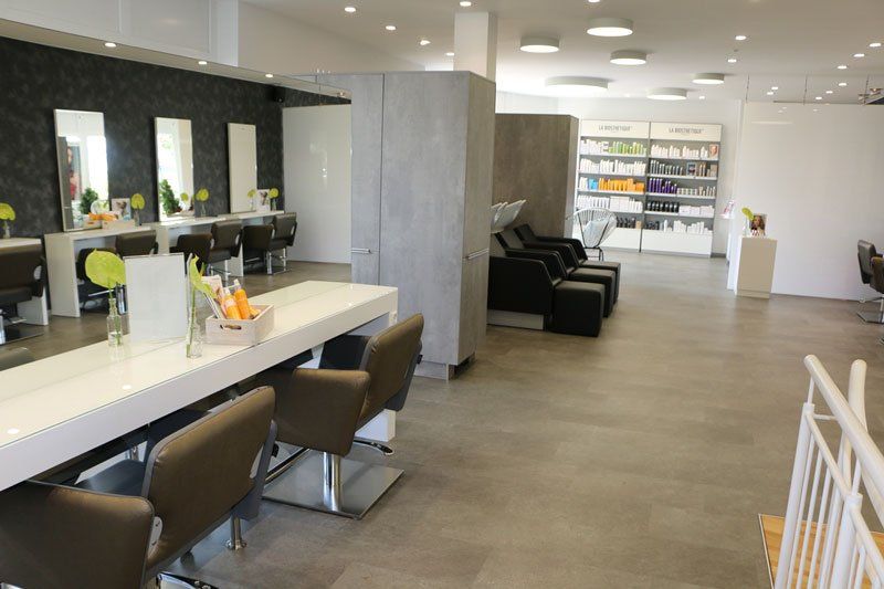 Inneneinrichtung eines Friseursalons mit Stationen, Stühlen, Spiegeln und Produktpräsentation.