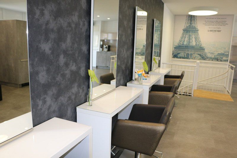 Friseursalon mit dunkelgrauer strukturierter Wand, weißen Theken, Spiegeln und braunen Stühlen. Wandgemälde des Pariser Eiffelturms.