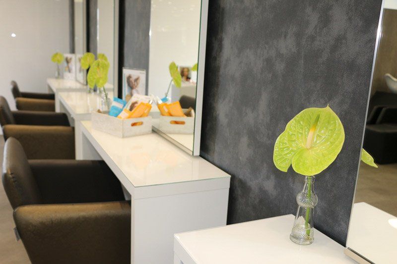 Friseursalon-Interieur mit Stühlen, Spiegeln und dekorativen Blumen in einer Reihe.