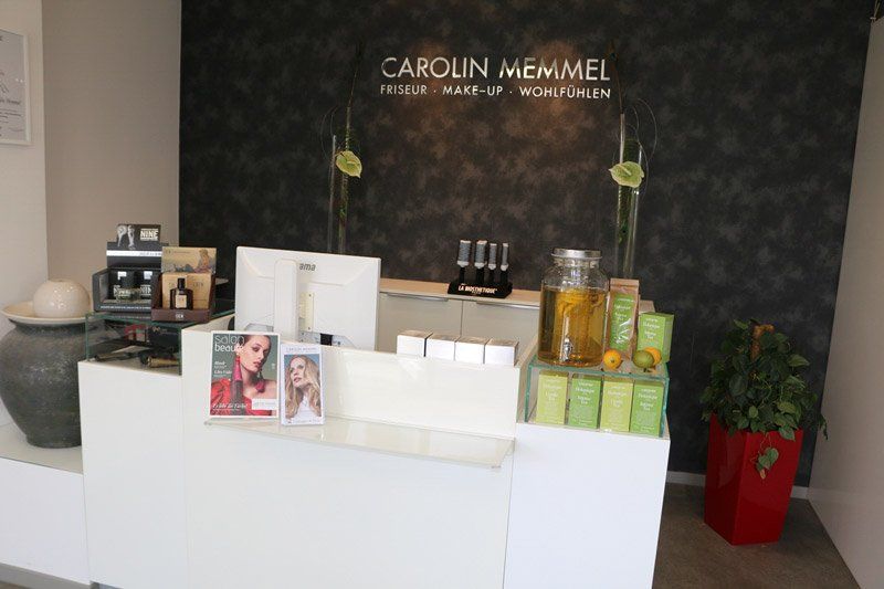 Weißer Salon-Rezeptionstresen mit Produkten, schwarzer Wand und einer Pflanze.