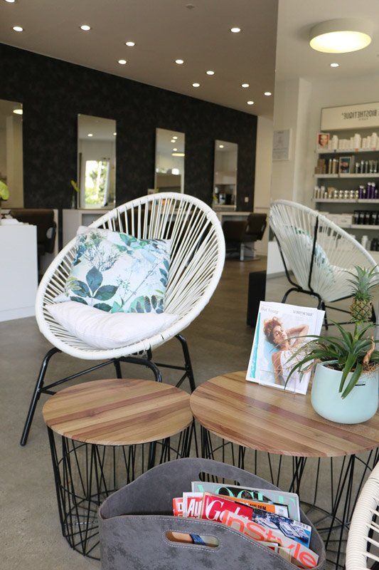 Wartebereich eines Friseursalons mit weißen Stühlen, Holztischen und Dekor.