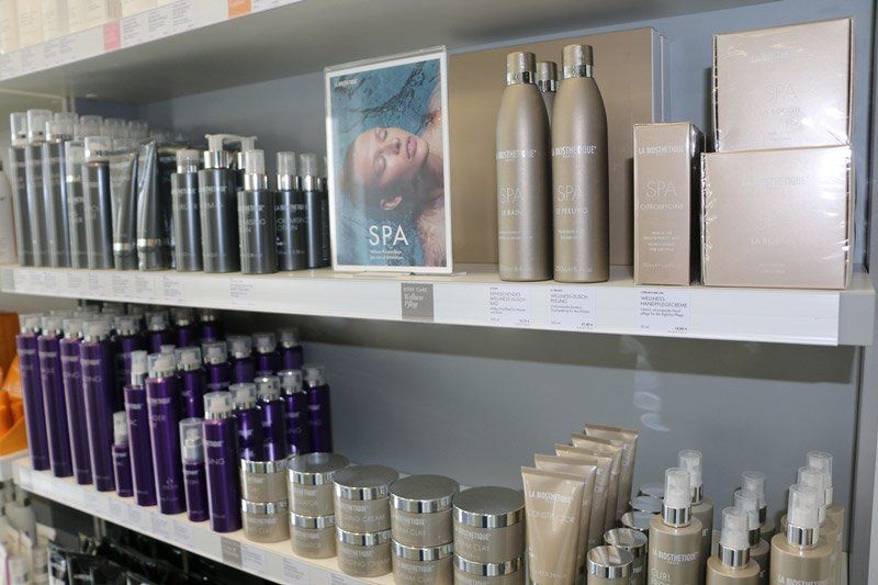 Regale mit verschiedenen Hautpflege- und Haarprodukten, darunter Flaschen, Tiegel und Tuben. Auf dem Schild steht „SPA“.