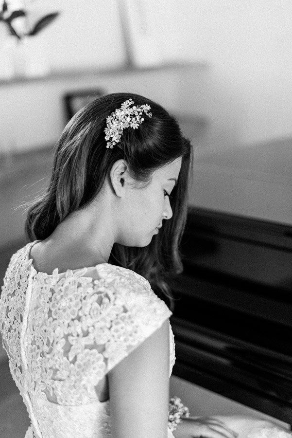 Frau mit juwelenbesetztem Haarteil spielt Klavier und trägt ein Spitzenkleid. Schwarzweißfoto.