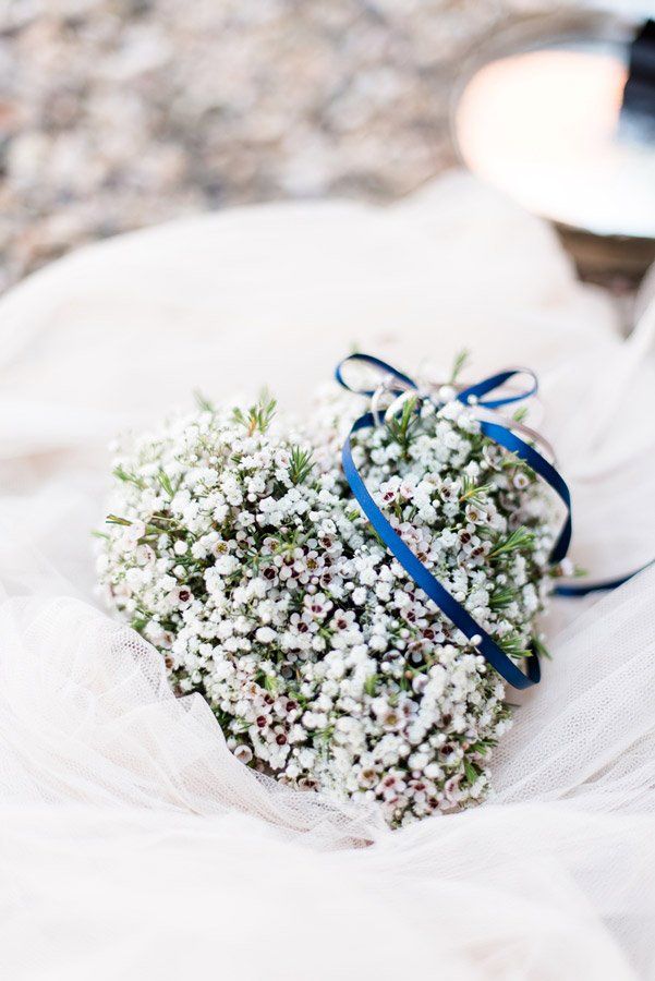 Herzförmiger Strauß weißer Blumen, mit blauem Band zusammengebunden, auf weißem Stoff.