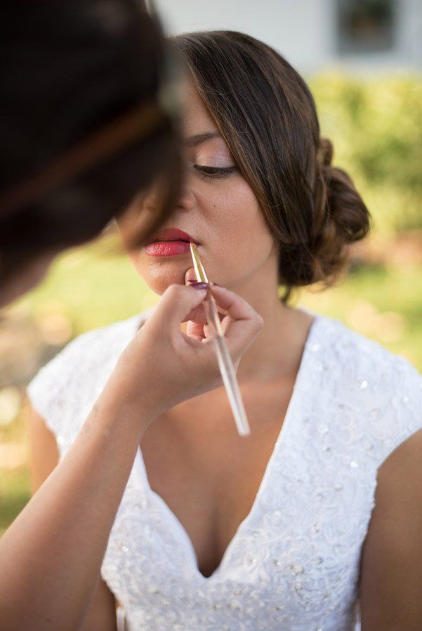 Eine Braut in einem weißen Kleid lässt sich von einem Visagisten Lippenstift auf die Lippen auftragen.