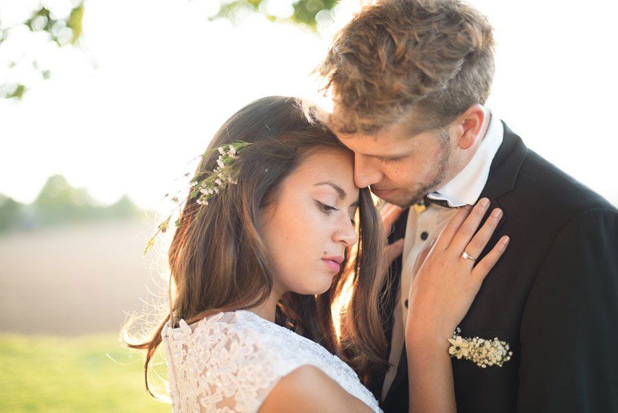 Braut und Bräutigam umarmen sich im Freien. Braut im weißen Spitzenkleid, Bräutigam im Smoking. Goldenes Sonnenlicht.