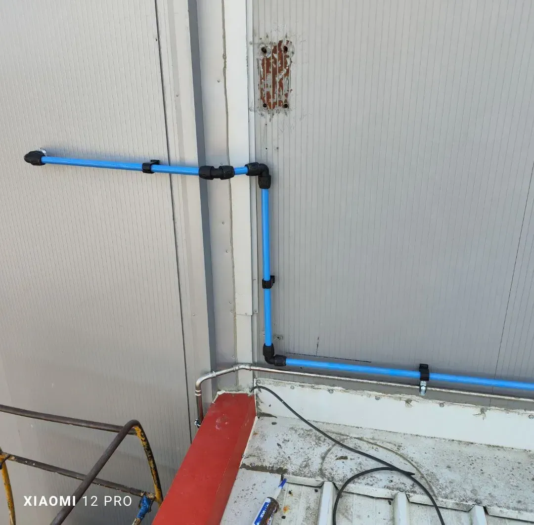 Un tubo azul recorre la esquina de una pared, por encima de un tubo rojo y de los cables del suelo dentro de una habitación.