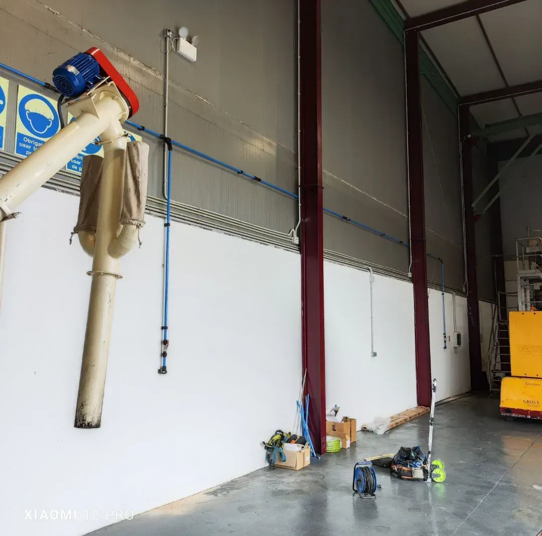 Interior de un almacén industrial con equipos de limpieza, paredes blancas y un ascensor amarillo a lo lejos.