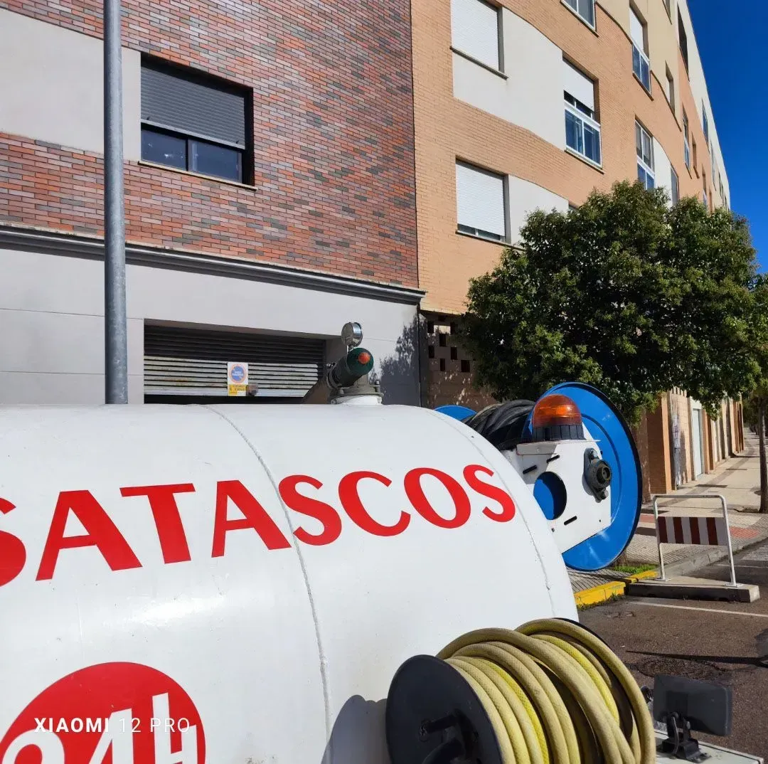Trabajador junto a un camión cisterna blanco de SATASCOS en una calle de la ciudad frente a un edificio de apartamentos.