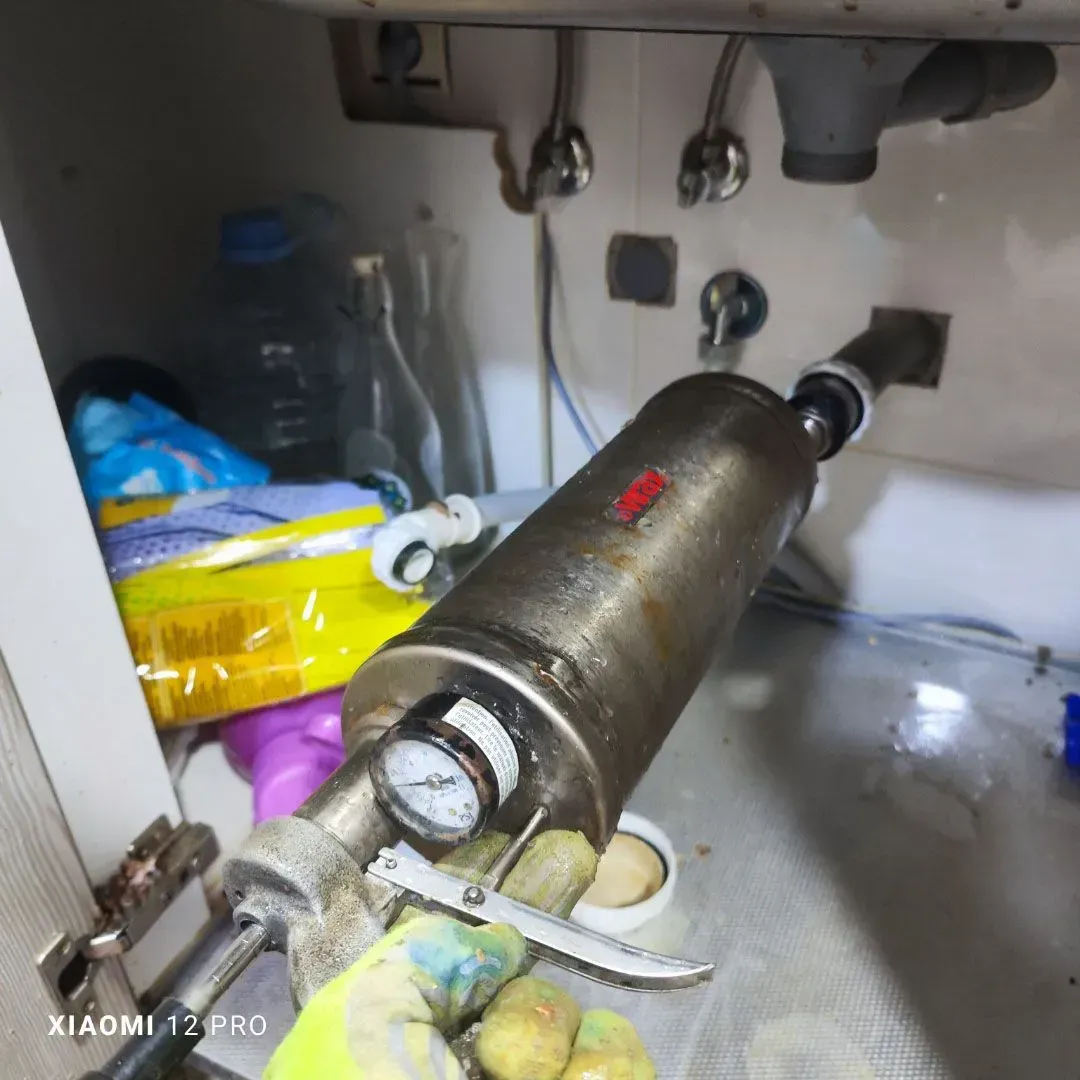Un mortero de metal sobre una encimera debajo del fregadero, con fruta y bolsas al fondo.