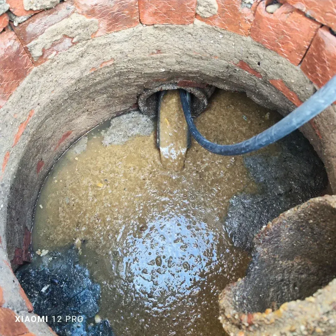 Pozo de ladrillo con agua turbia, una manguera azul y una abertura para tubería en el interior del pozo.