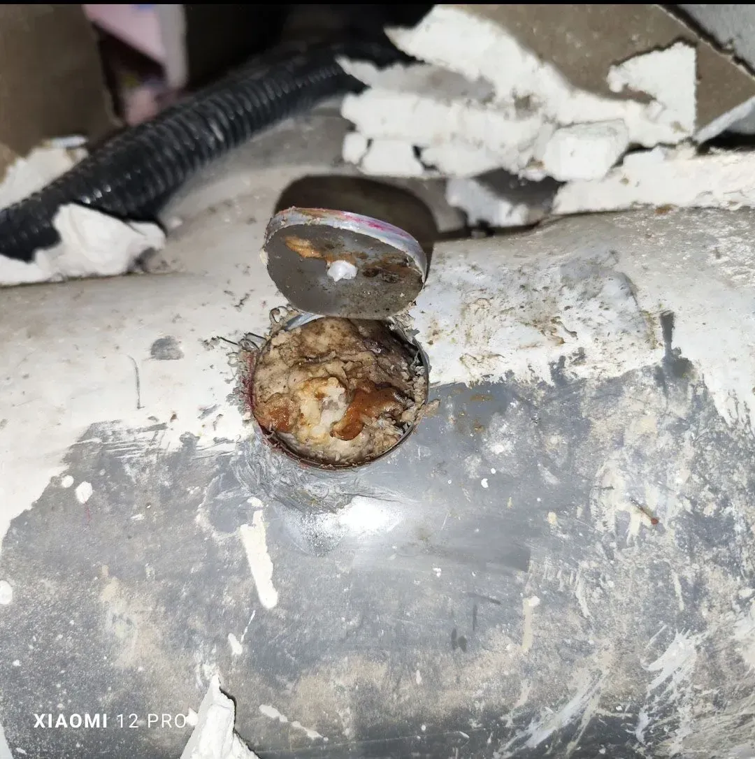 Primer plano de una superficie metálica corroída con un perno dañado y restos blancos desprendidos cerca.