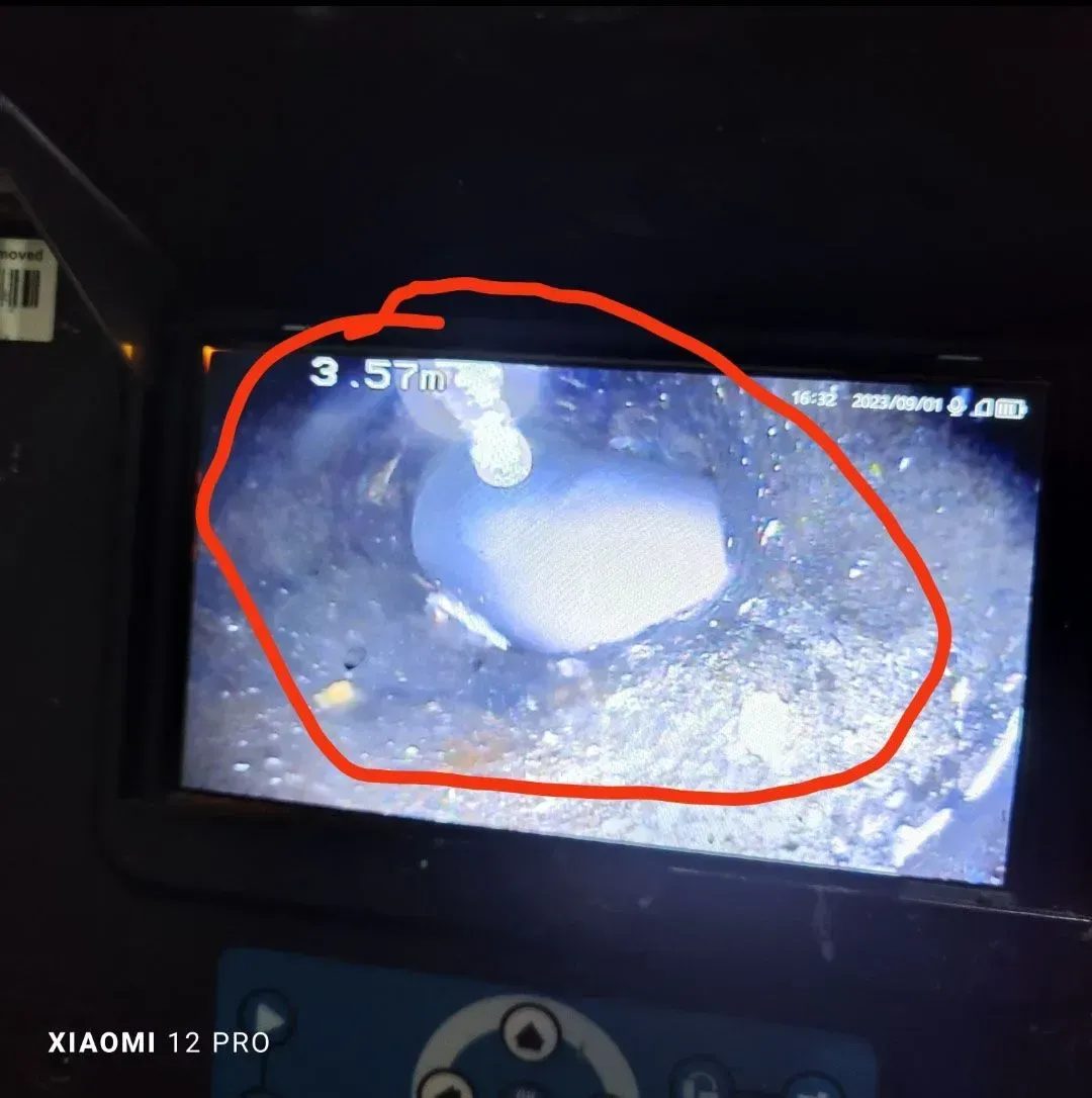 La pantalla de una cámara muestra un objeto redondo y gris sobre una superficie rugosa, rodeado por un círculo rojo.
