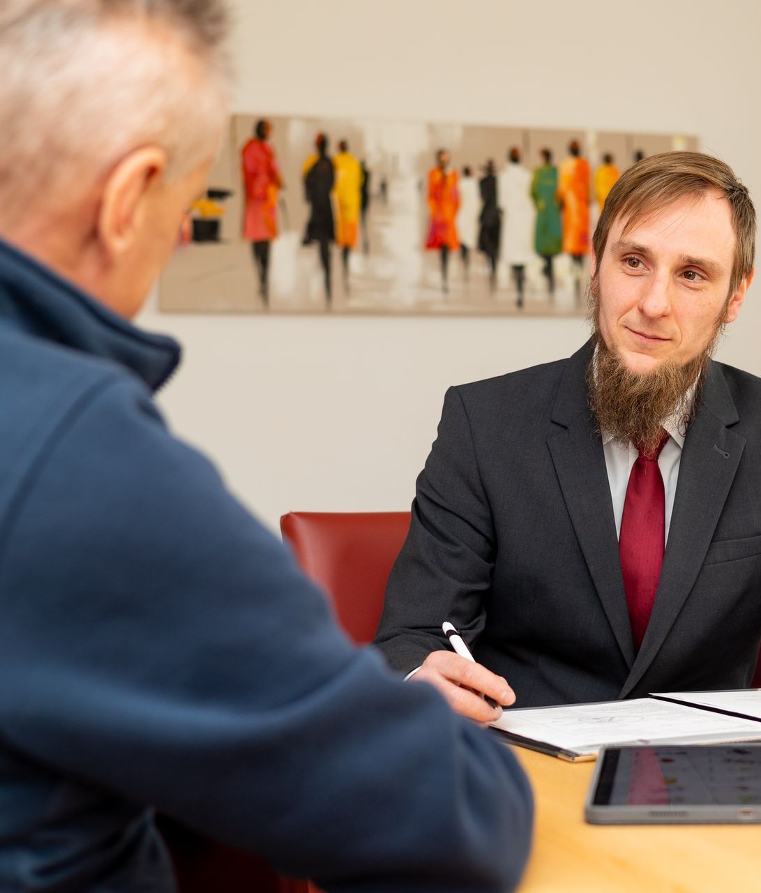 Ein Mann in Anzug und Krawatte sitzt an einem Tisch und unterhält sich mit einem anderen Mann