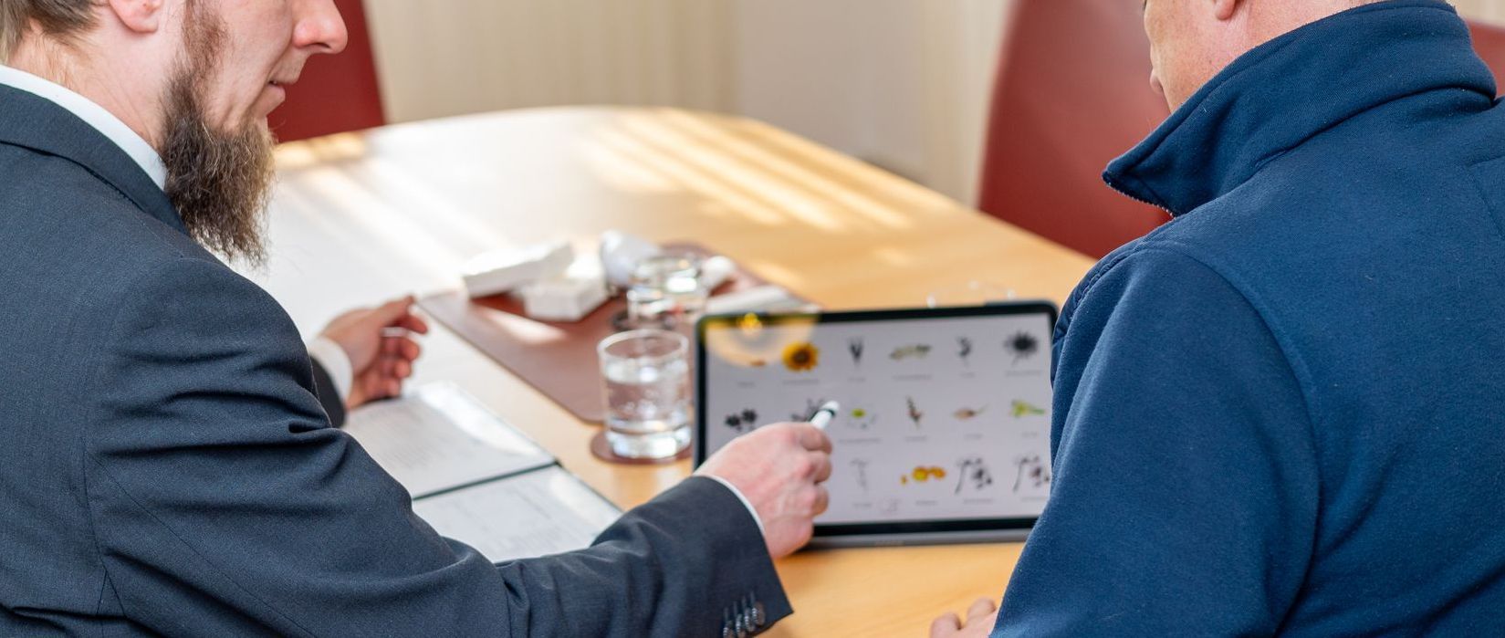 Zwei Männer sitzen an einem Tisch und schauen auf ein Tablet.