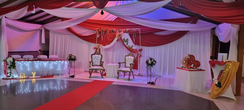 Un espace événementiel décoré avec des tentures rouges et blanches au plafond, deux chaises, un tapis rouge et des guirlandes lumineuses.