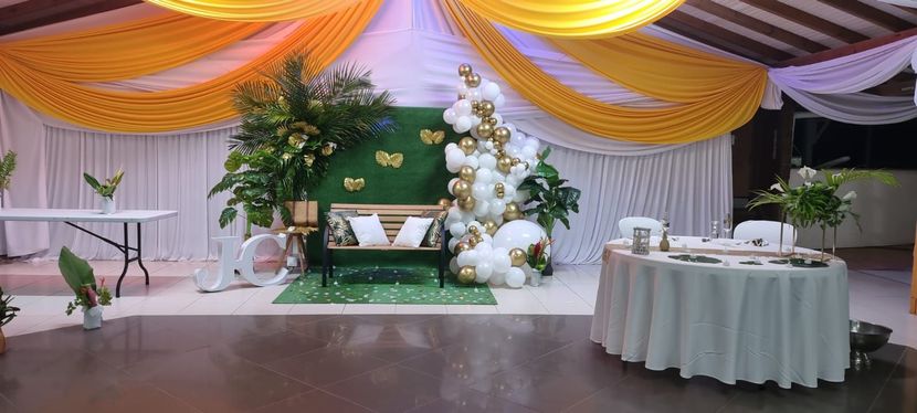 Un espace événementiel décoré avec des plafonds drapés jaunes et blancs, un coin photo central avec banc, verdure et ballons.