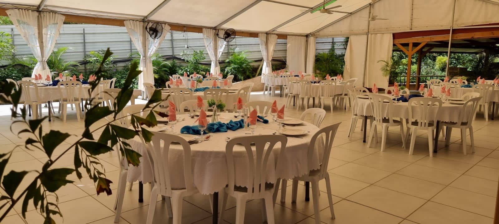Une tente blanche installée pour un événement, avec plusieurs tables rondes recouvertes de nappes blanches, des serviettes roses et des chaises.