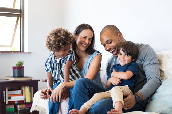Une famille est assise ensemble sur un canapé, souriant et riant dans un cadre intérieur lumineux et décontracté.