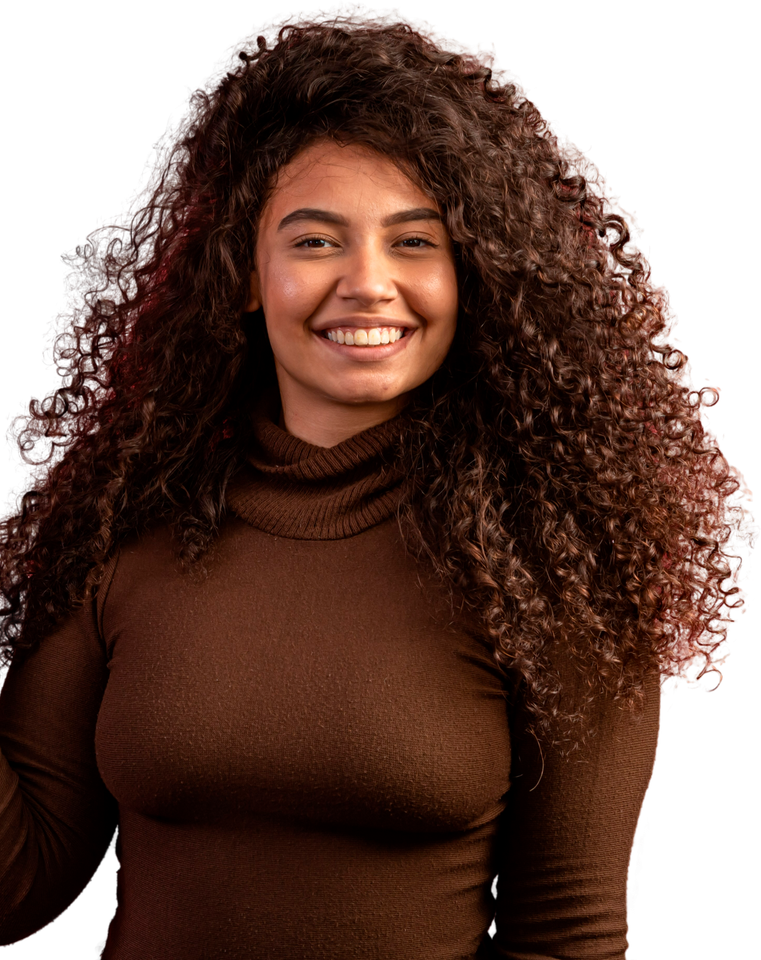 Une personne souriante aux longs cheveux bouclés et volumineux porte un pull à col roulé marron sur un fond blanc uni.