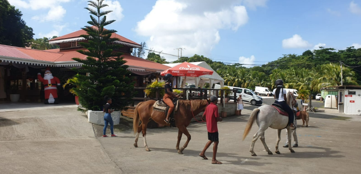 Deux personnes chevauchent le long d'une plage tropicale ensoleillée, près des montagnes et de la mer.