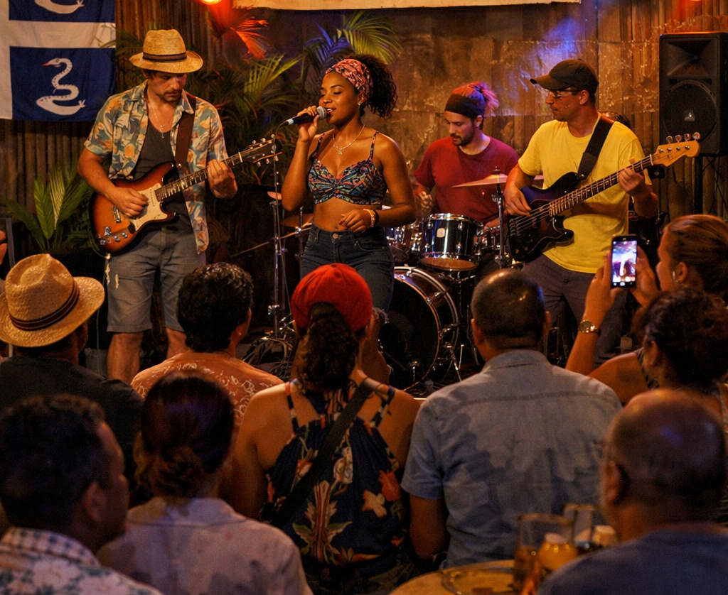 Un groupe se produit sur une petite scène intérieure devant un public, avec un chanteur, deux guitaristes et un batteur.